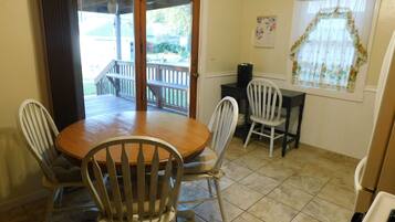 A dining area with a wooden table and four chairs, a black coffee machine, and a window with a floral curtain.