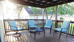 Une terrasse couverte avec quatre chaises et une table, entourée d’une balustrade en bois.