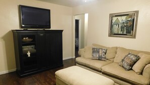 Un salon avec un meuble en bois foncé, un canapé beige orné de coussins à motifs et un téléviseur à écran plat posé sur le dessus.
