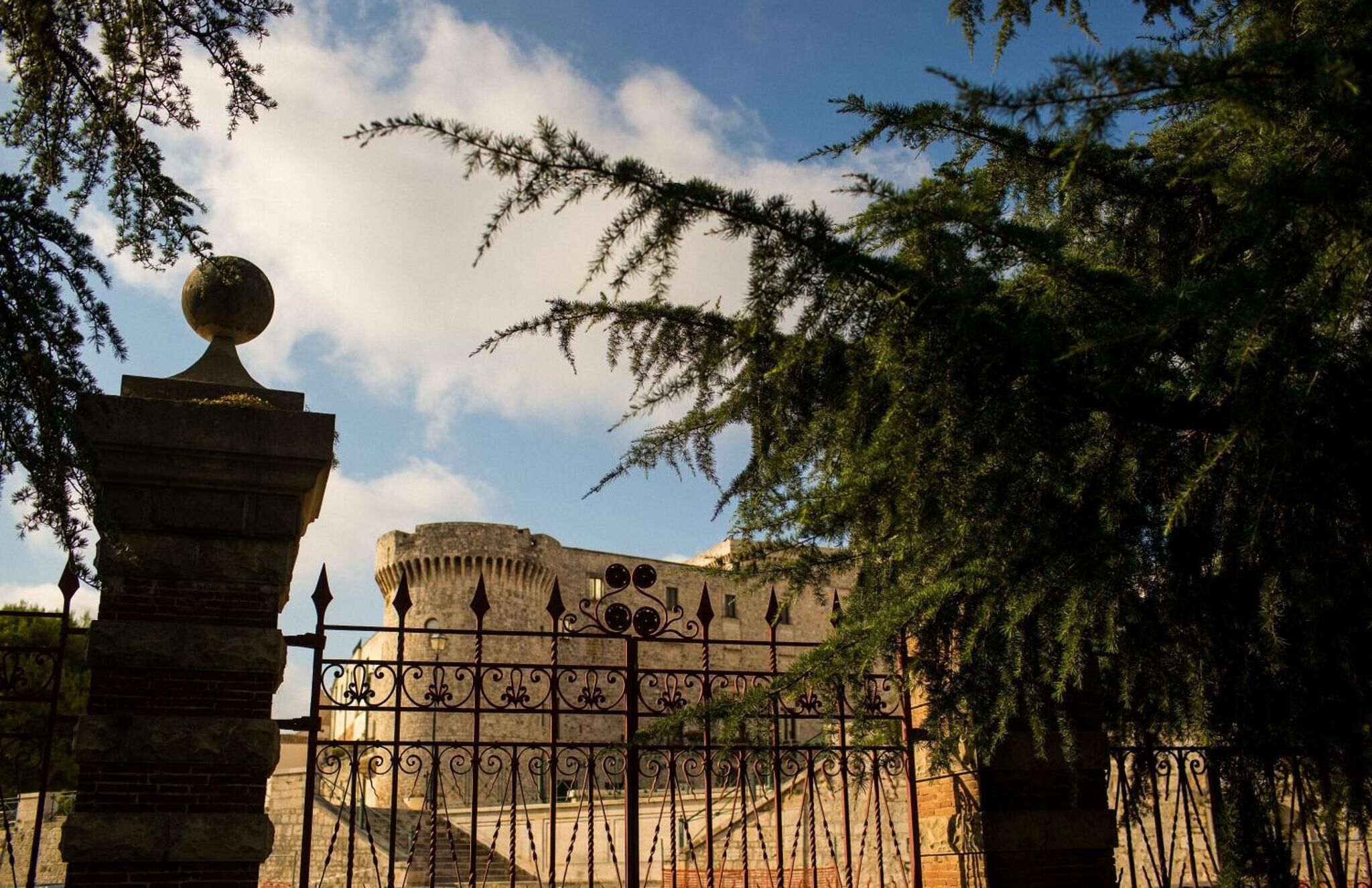 A historic building with a stone facade, a round dome, and a gate with decorative ironwork.