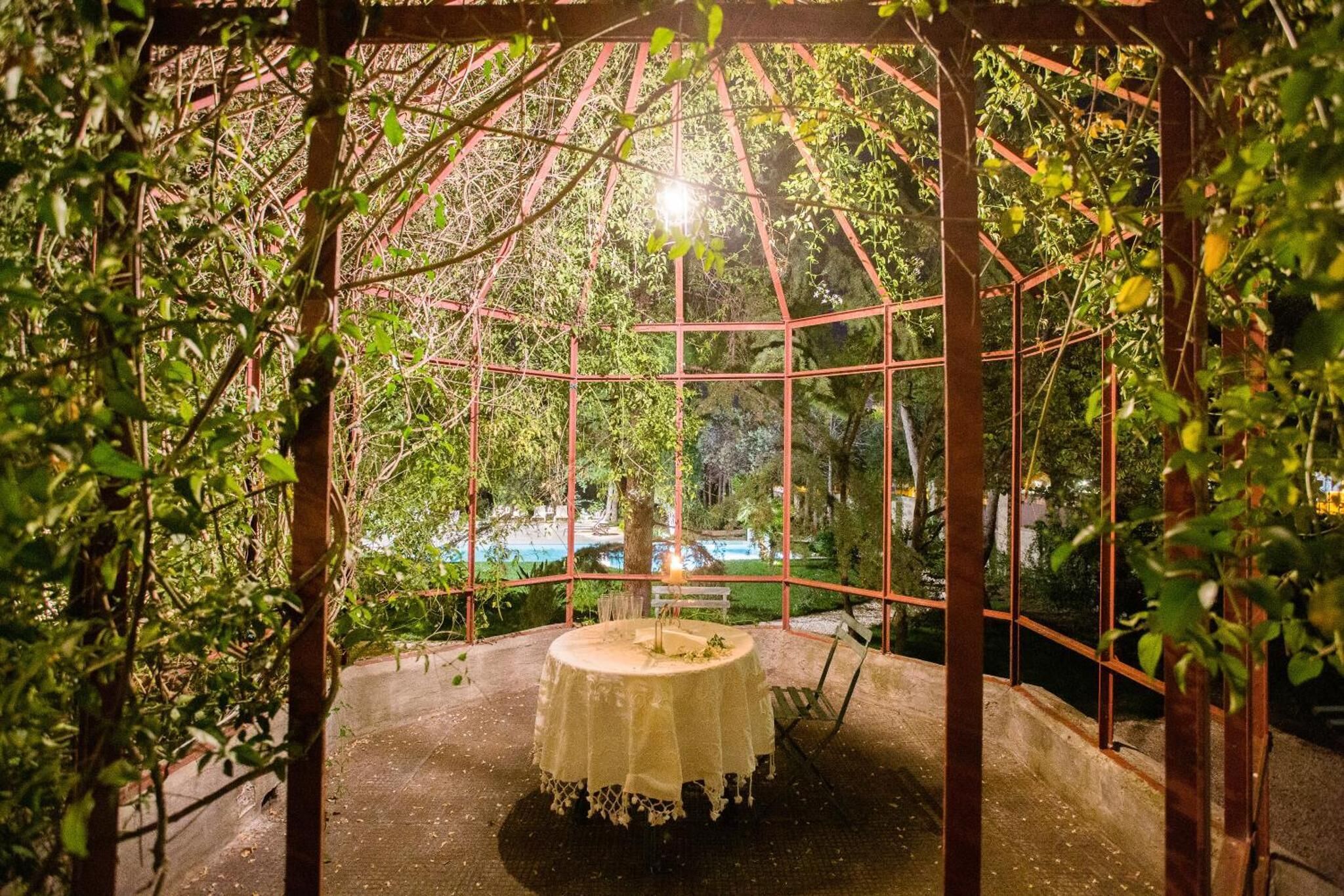 A gazebo with a table and chairs, surrounded by greenery and a view of a body of water.