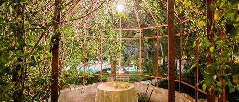 A gazebo with a table and chairs, surrounded by greenery and a view of a body of water.