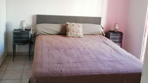 A bedroom with a large bed, two bedside tables, a red hanging lamp, and a window with curtains.