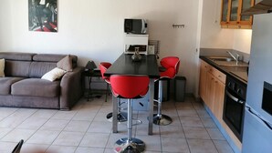 A compact living space with a kitchenette, a dining area with two red chairs, a sofa, and a TV.