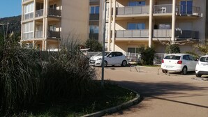A multi-story residential building with balconies, a parking area, and a clear sky.