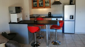 A compact kitchen with a central island, red bar stools, a microwave, a coffee maker, and a refrigerator.