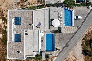 Une maison moderne à deux étages dotée d’une grande piscine, d’un espace extérieur aménagé et d’un patio couvert.