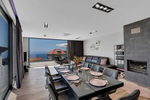 Un espace de repas moderne avec une longue table dressée pour six personnes, une cheminée et une vue sur la mer.