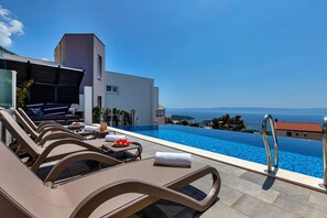 Une piscine à débordement moderne, dotée de chaises longues et offrant une vue sur la mer.