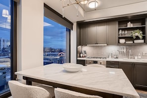 A modern kitchen with a large window, a marble countertop, and dark cabinetry. - Luxury Furnished Condo in the Iconic Coloradan Live in the Heart of Denver! (Denver)