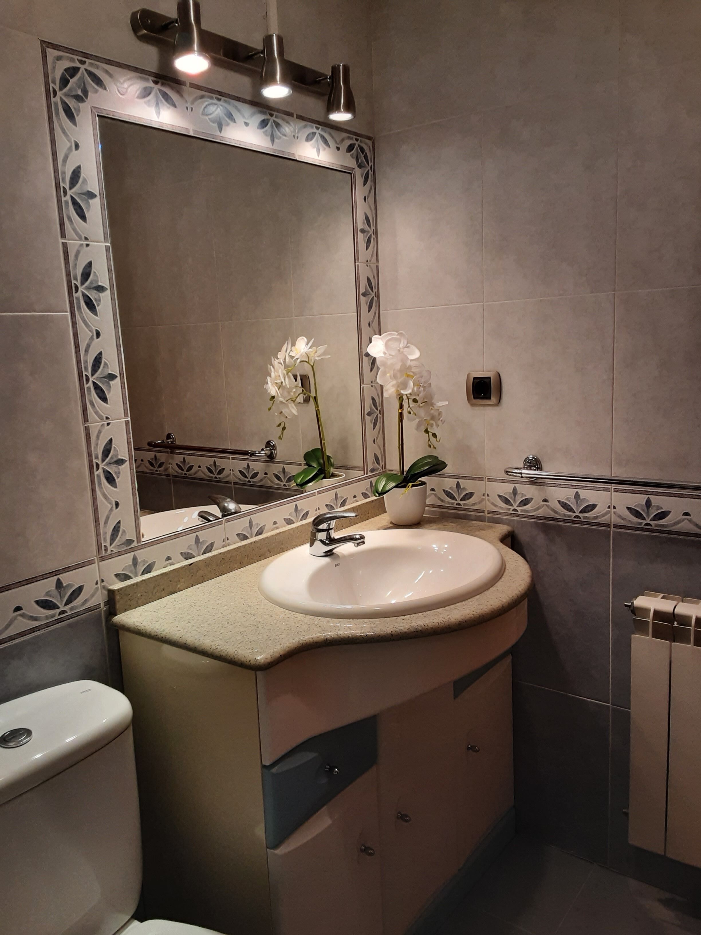 Een badkamer met een wit wastafelmeubel, een spiegel met decoratieve lijst en een toilet.
