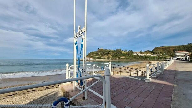 Un paseo marítimo con un flotador salvavidas, un letrero que dice "Rampa" y vistas de la playa y el océano.