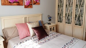 Un dormitorio con cama, almohadas, mesita de noche, lámpara y armario.