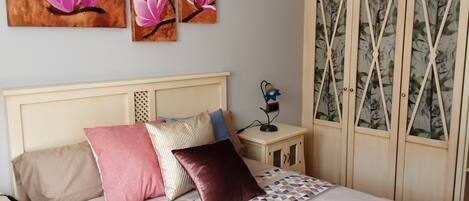 A bedroom with a bed, pillows, a nightstand, a lamp, and a wardrobe.