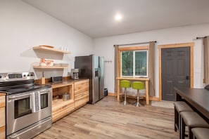 Eine moderne Küche mit Edelstahlgeräten, Holzschränken und einem Essbereich mit zwei grünen Stühlen.