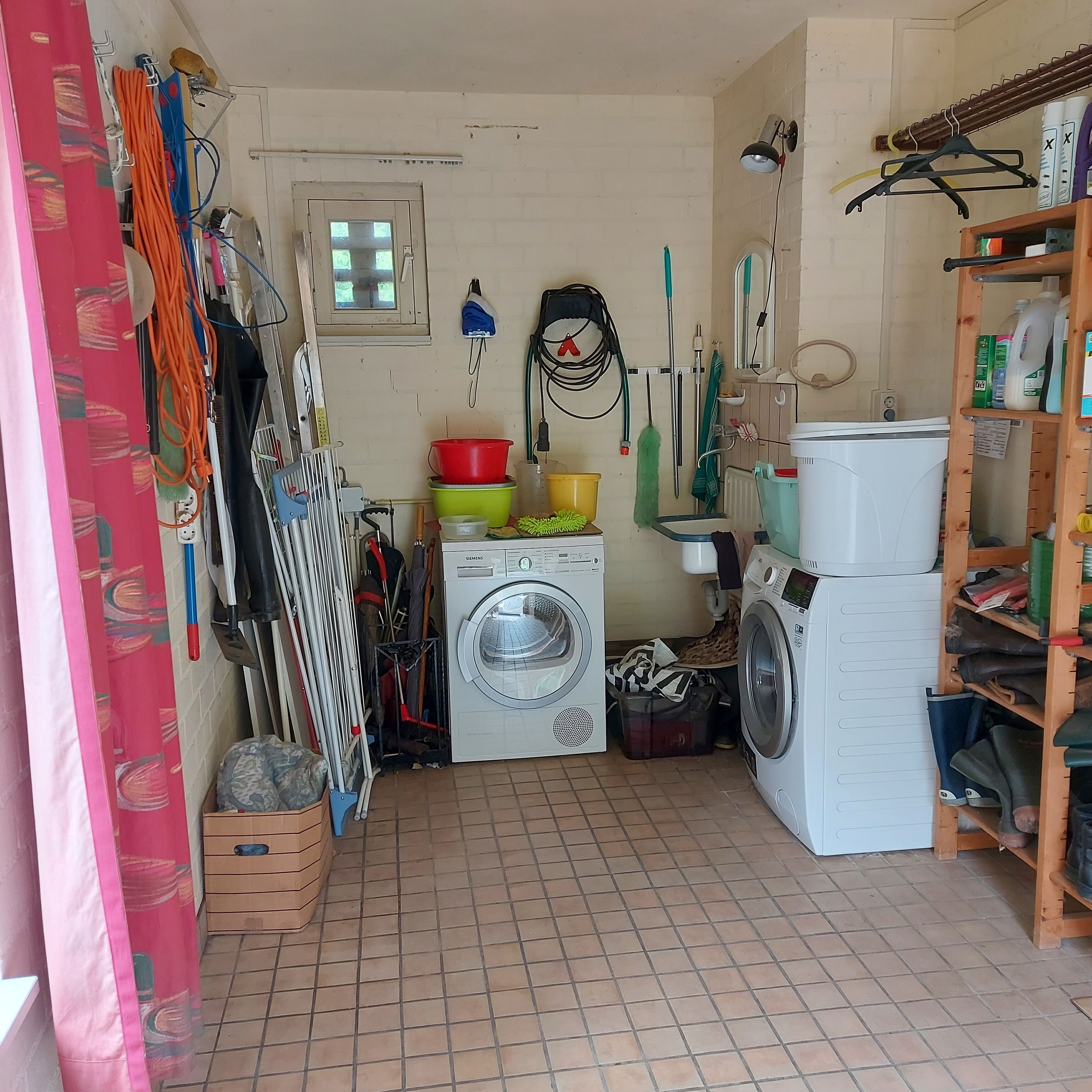 A laundry room with two washing machines, a drying rack, and various cleaning supplies.
