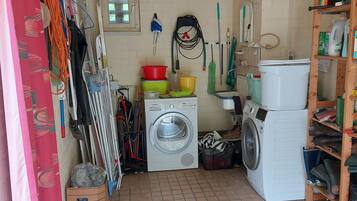 A laundry room with two washing machines, a drying rack, and various cleaning supplies.