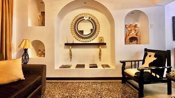 A room with a sofa, a chair, a mirror, and a fireplace.