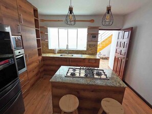 A modern kitchen with wooden cabinets, a gas stove, and two stools. - Luxury 2BR/2BA w/ Jacuzzi - Walk to Beach & Castle (Chancay)