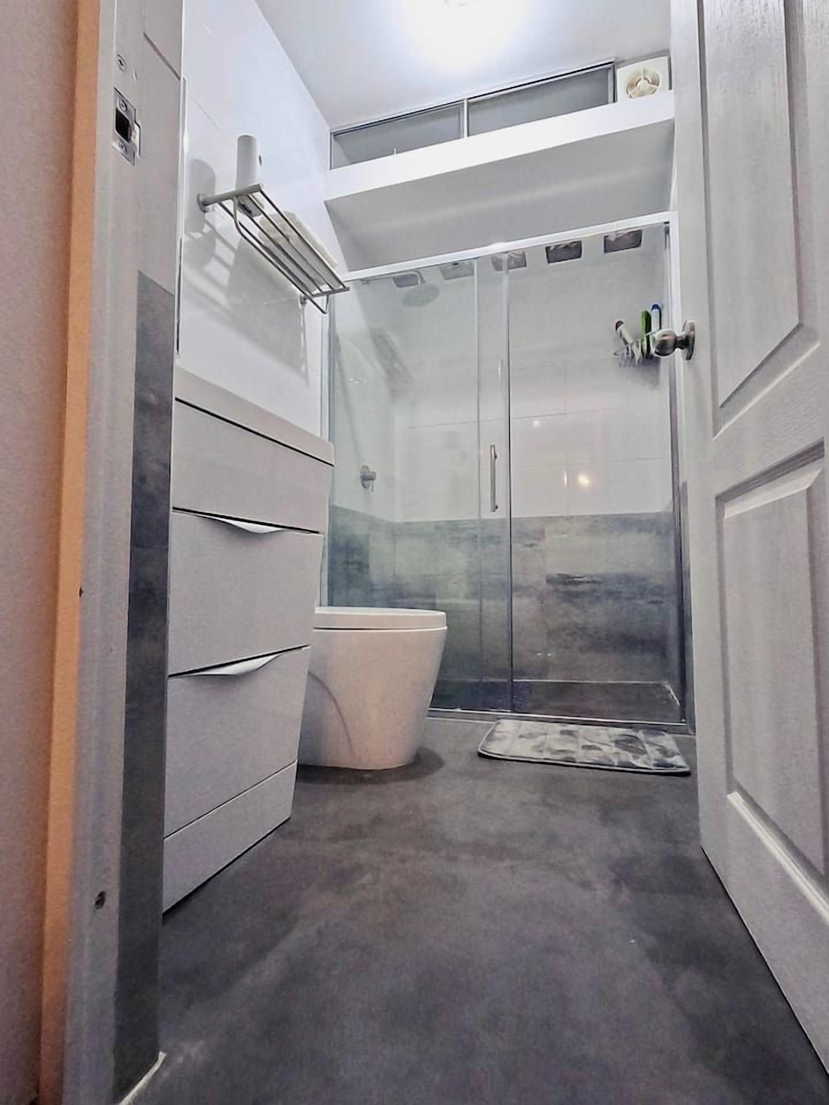 A bathroom with a glass shower enclosure, a toilet, and a towel rack.
