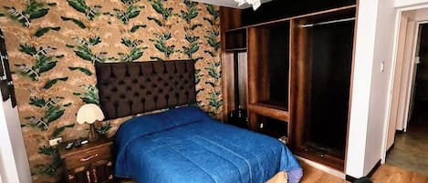 A bedroom with a bed, a nightstand, a lamp, a chair, and a wardrobe.