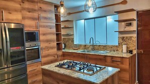 A modern kitchen with wooden cabinets, stainless steel appliances, a gas stove, and pendant lighting. - Luxury 2BR/2BA w/ Jacuzzi - Walk to Beach & Castle (Chancay)