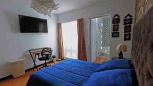 A bedroom with a bed, a desk, a chair, a television, and a window with curtains.