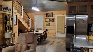 Un interior acogedor de estilo cabaña, con una escalera de madera, una zona de comedor y una cocina moderna con refrigerador de acero inoxidable.