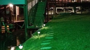 Vista nocturna de un edificio con terraza de madera y una escalera que sube a un segundo nivel.