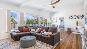 Amplia sala de estar con sofá modular, reposapiés y ventanas grandes.