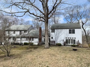 A two-story white house with a large front yard, a tree, and a small pond.