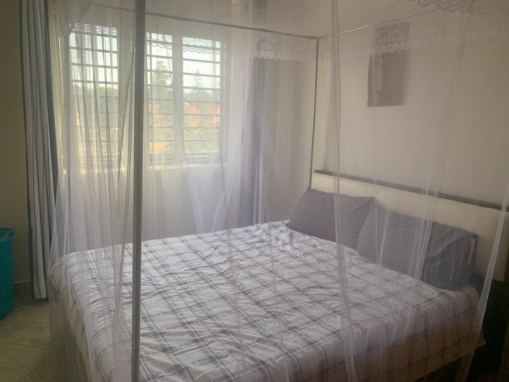 Ein Schlafzimmer mit einem Moskitonetz über dem Bett, einem Fenster mit Vorhängen und einem kleinen, an der Wand befestigten Regal.