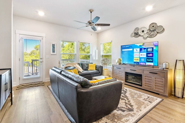 A living room with a sofa, television, ceiling fan, and decorative wall art.