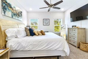 Un dormitorio con cama, ventilador de techo, televisor, cómoda y ventana con persianas.