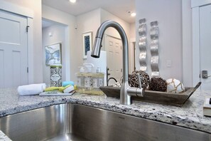 A modern kitchen with a stainless steel sink, a silver faucet, and a decorative bowl with wicker and a decorative egg. - Modern 4BR Retreat • Walk to Beach • Private King Suites • Pet-Friendly (Perdido Key)