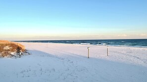 Una playa nevada con un camino de madera y señalizaciones.