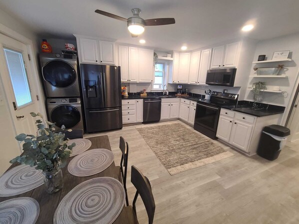 A modern kitchen with white cabinets, stainless steel appliances, and a dining area with a wooden table and chairs.