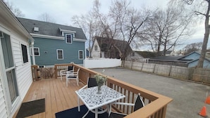 Une terrasse en bois avec une table et des chaises, un petit jardin et une vue sur les maisons voisines.