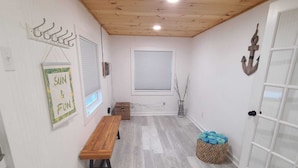 Une pièce avec un plafond en bois, un banc, un panneau mural avec des crochets, une fenêtre avec des stores et une porte dotée de panneaux de verre.