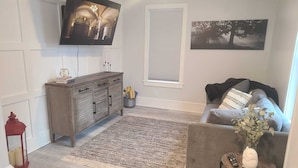 Un salon avec un canapé gris, un meuble en bois, un téléviseur à écran plat, un tapis à motifs et un tableau accroché au mur.