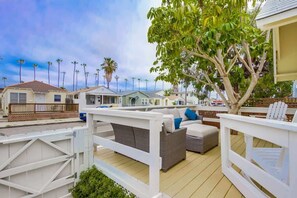 A deck with outdoor furniture, a white fence, and a tree. - Beach Daze Large (San Diego)