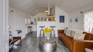 Una sala de estar moderna con un sofá marrón, una mesa de centro redonda con un florero y una cocina al fondo.