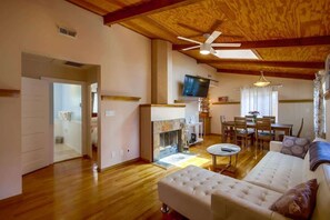 A spacious living room with a fireplace, a ceiling fan, a television, and a dining area with wooden furniture.