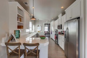 A kitchen with white cabinets, a stainless steel refrigerator, a microwave, and a large island with two wooden chairs.