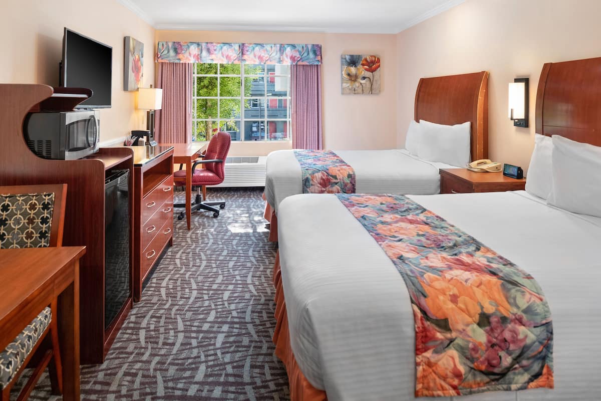 A hotel room with two beds, a desk with a TV, a chair, and a window with curtains.