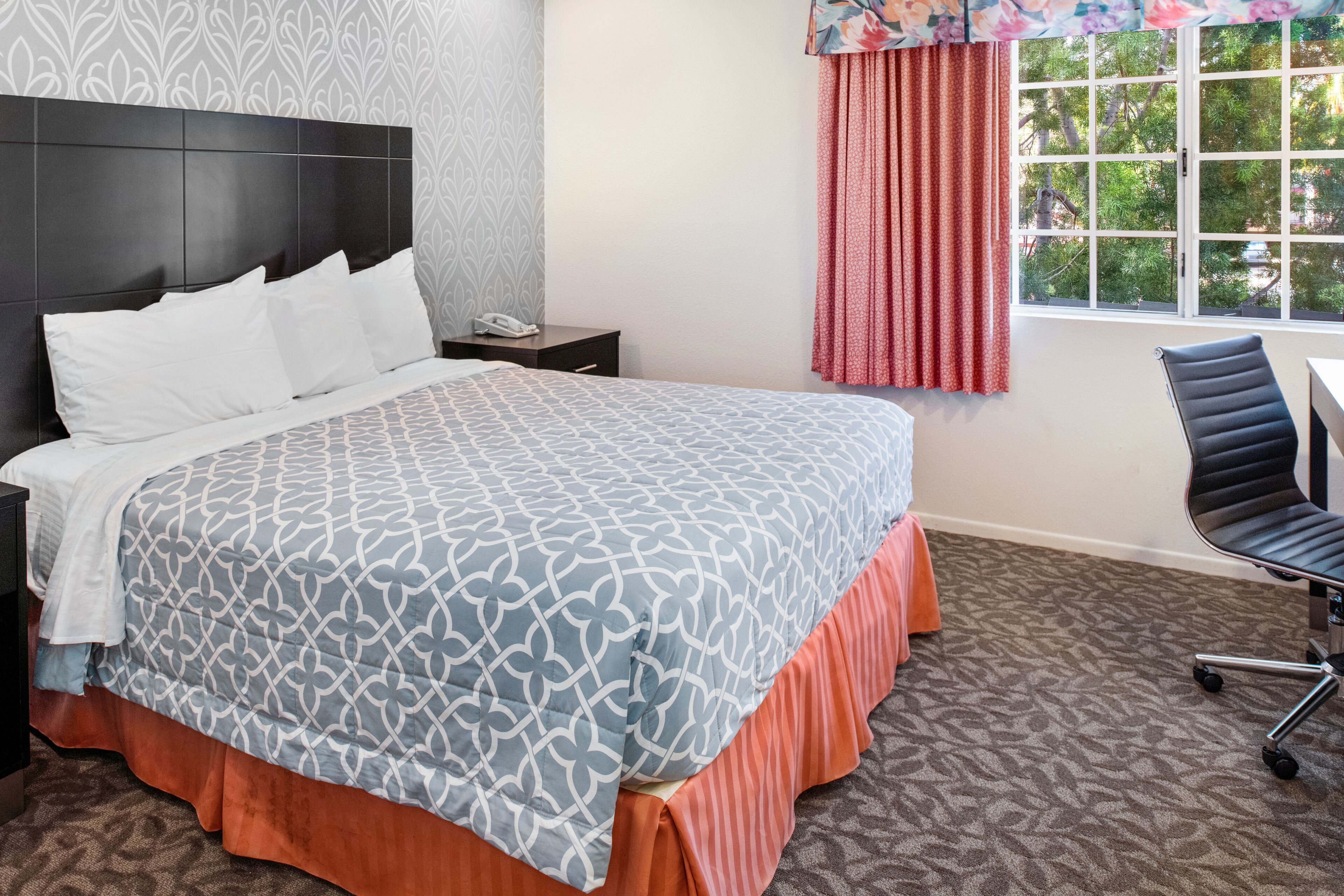 A hotel room with a large bed, a nightstand, a desk, and a chair.