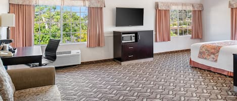 A hotel room with a bed, a desk with a chair, a flat-screen TV, a microwave, and a large window with curtains.