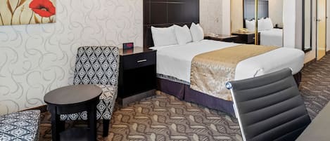 Ein Hotelzimmer mit einem großen Bett, einem Nachttisch, einem Sessel, einem kleinen Tisch und einem Spiegel.
