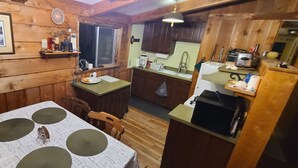 Interior de una cabaña de madera con una mesa de comedor, sillas, una zona de cocina con un fregadero y un refrigerador.