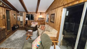 Una sala de estar acogedora con paredes de madera, un televisor de pantalla plana, un sofá, una mesa de centro y un ventanal corredero que da a un espacio exterior.